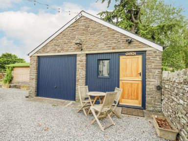 A stone building with blue garage doors and a wooden door with a small window and table with chairs outside at Ty Sinsir in Tretower