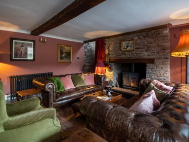 A living room with leather sofas, green armchair, stone fireplace, and paintings on the wall at Ty Sinsir in Tretower