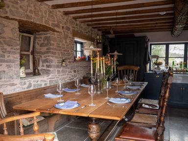 A dining room with a wooden table set with plates and wine glasses and stone walls at Ty Sinsir in Tretower