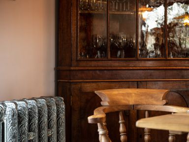 An ornated metal radiator next to a wooden chair with a round backrest and a wooden cabinet with glass doors containing glassware at Ty Sinsir in Tretower