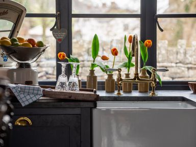 A kitchen sink with a brass faucet and orange tulips in vases on the windowsill at Ty Sinsir in Tretower