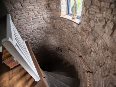 A spiral stone staircase with a rope handrail and a statue on a window ledge at Ty Sinsir in Tretower