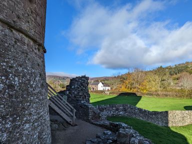 A stone building with wooden stairs and stone walls in a grassy area with houses and trees in the background at Ty Sinsir in Tretower