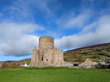 A ruined stone castle tower in a green field with farm buildings and hills in the background at Ty Sinsir in Tretower