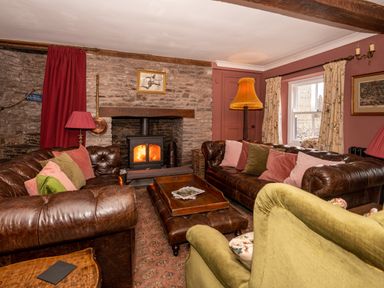 A living room with leather sofas a green armchair a wood burning stove and cushions at Ty Sinsir in Tretower