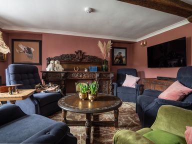 A living room with blue and green armchairs a carved wooden desk wooden coffee table and paintings on pink walls at Ty Sinsir in Tretower