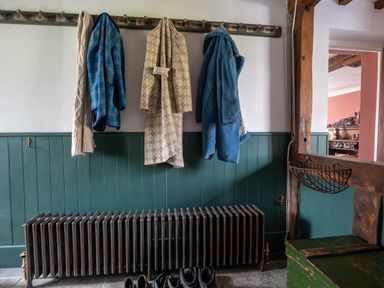A hallway with coats hanging on hooks above a radiator and shoes on the floor at Ty Sinsir in Tretower