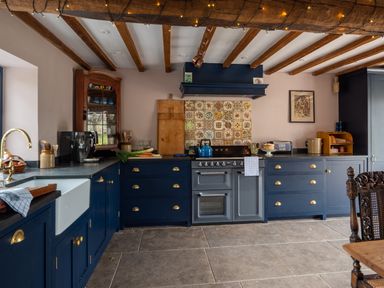 A kitchen with dark blue cabinets a farmhouse sink a stove with a tiled backsplash and wooden ceiling beams at Ty Sinsir in Tretower