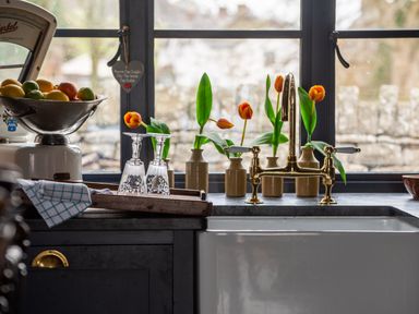 A kitchen sink with brass faucet and vases with orange tulips on the windowsill at Ty Sinsir in Tretower