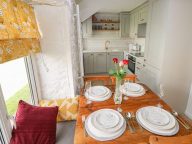 A kitchen with light gray cabinets and white tiled backsplash a wooden dining table set for four with plates cutlery and glasses at Primrose Cottage in Manorbier