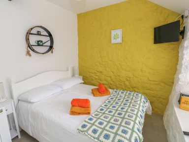 A bedroom with a double bed white bedding towels on bed yellow textured wall and wall-mounted tv at Primrose Cottage in Manorbier