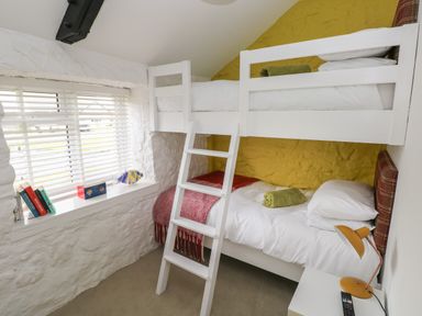 A bedroom with a white bunk bed a window with blinds and books on the windowsill at Primrose Cottage in Manorbier