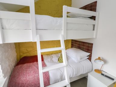 A bedroom with white bunk beds a red blanket a yellow wall a bedside table with a lamp and remote at Primrose Cottage in Manorbier