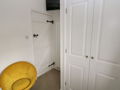 A corner of a room with a white door with black hinges a yellow chair and white closet doors at Primrose Cottage in Manorbier