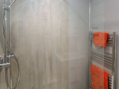 A shower area with a handheld showerhead and a towel rack with orange towels at Primrose Cottage in Manorbier