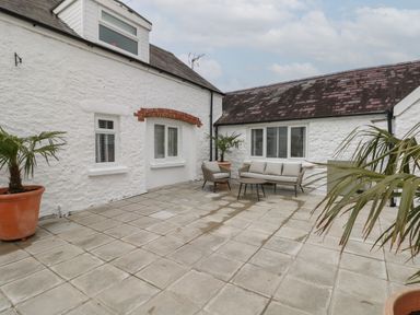An outdoor patio with tiled floor seating area and potted plants at Primrose Cottage in Manorbier