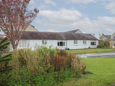 A white stone cottage with multiple windows and a dark roof surrounded by a garden and lawn at Primrose Cottage in Manorbier