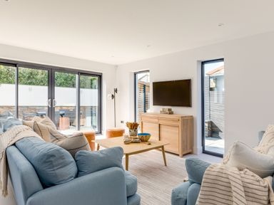 A living room with blue sofas a wooden coffee table and a wall mounted television at 12 Tintagel Terrace in Port Isaac