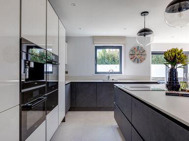 A modern kitchen with black and white cabinets a window above a sink and a kitchen island with flowers at 12 Tintagel Terrace in Port Isaac