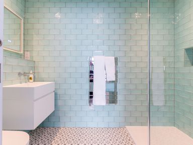 A bathroom with a white sink, a mirror, a tiled wall, a towel rack with white towels, and a glass shower enclosure at 12 Tintagel Terrace in Port Isaac
