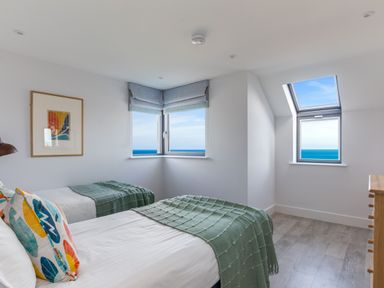 A bedroom with two single beds green blankets and colorful pillows with ocean views at 12 Tintagel Terrace Port Isaac