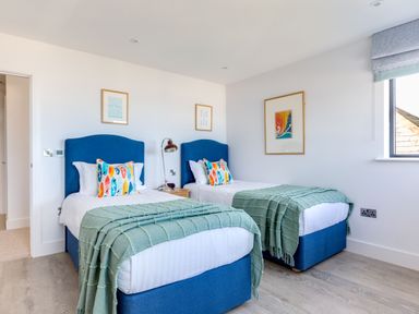 A bedroom with two single beds blue headboards colorful pillows green blankets and framed pictures at 12 Tintagel Terrace in Port Isaac