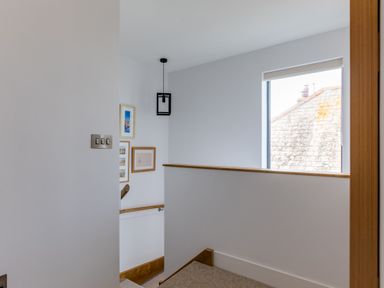A stairway area with framed pictures on the wall a hanging light and a window showing a roof at 12 Tintagel Terrace Port Isaac