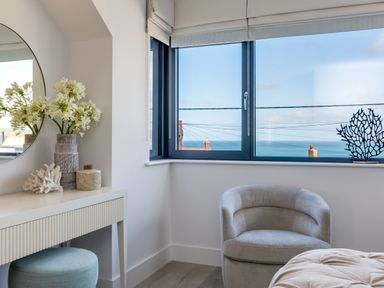 A corner of a room with a round mirror on a table with decorative items and a window with a view of the sea at 12 Tintagel Terrace in Port Isaac