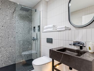A bathroom with a shower area, toilet, black sink, round mirror, and white towels at 12 Tintagel Terrace in Port Isaac
