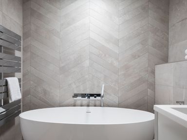 A bathroom with a white freestanding bathtub and a chrome faucet against tiled walls at 12 Tintagel Terrace Port Isaac