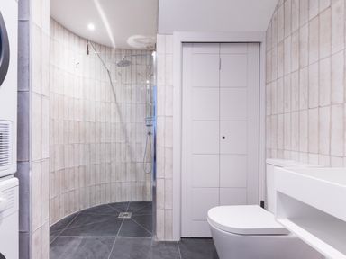 A bathroom with a curved tiled shower enclosure a toilet a white door and a washing machine at 12 Tintagel Terrace in Port Isaac