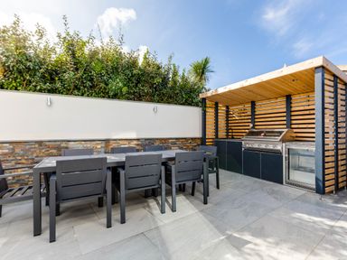 An outdoor dining area with black chairs and table next to a covered section with a grill sink and refrigerator at 12 Tintagel Terrace in Port Isaac
