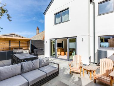 An outdoor patio with a gray sofa wooden chairs a dining table with chairs and a barbecue grill at 12 Tintagel Terrace in Port Isaac