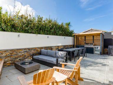 An outdoor patio with wooden chairs a gray sofa a fire pit a dining table with chairs and a covered barbecue area at 12 Tintagel Terrace in Port Isaac