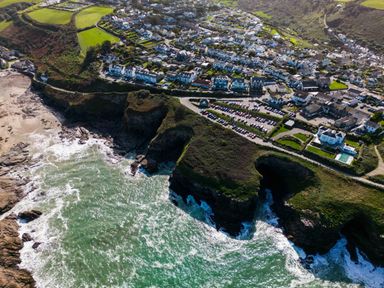 An aerial view of a coastal town with cliffs green fields houses and a parking lot at 12 Tintagel Terrace Port Isaac