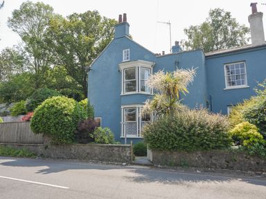 A blue house with bay windows and a garden with bushes and a stone wall at Braeside in Lyme Regis