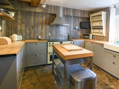 A kitchen with wooden countertops a central island stainless steel appliances and a small wall-mounted television at Braeside in Lyme Regis