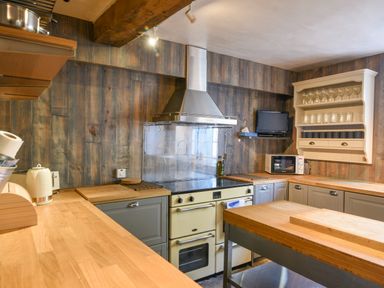 A kitchen with wooden countertops a stove a microwave and shelves with glasses at Braeside Lyme Regis