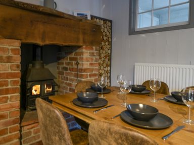 A dining table set with plates bowls wine glasses and cutlery near a brick fireplace with a wood burning stove at Braeside Lyme Regis
