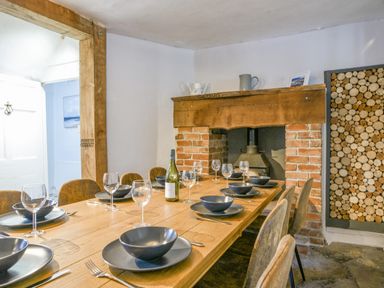 A dining room with a wooden table set with black bowls plates and wine glasses near a brick fireplace and a wood storage at Braeside Lyme Regis