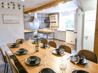 A kitchen with a wooden dining table set with plates bowls and wine glasses at Braeside Lyme Regis