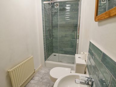 A bathroom with a shower enclosure a toilet a sink and a radiator with blue tiles on the walls at Braeside Lyme Regis