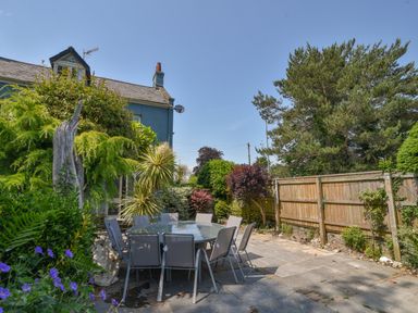 An outdoor patio area with a round glass table and chairs surrounded by various plants and a wooden fence at Braeside in Lyme Regis