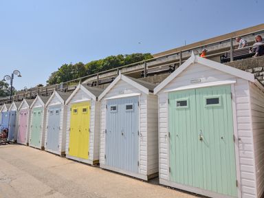 A row of colorful beach huts with numbered doors along a paved walkway