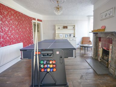 A room with a pool table, a small round table with a chair, a fireplace, and a white cabinet at Braeside Lyme Regis