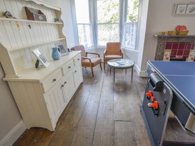 A room with two brown chairs around a glass table next to a white cabinet and a ping pong table at Braeside in Lyme Regis