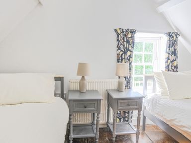 A bedroom with two single beds a window with curtains and two bedside tables with lamps at Braeside Lyme Regis