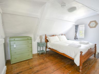 A bedroom with a wooden bed, bedside tables with lamps, a green chest of drawers, and a window with a curtain at Braeside in Lyme Regis