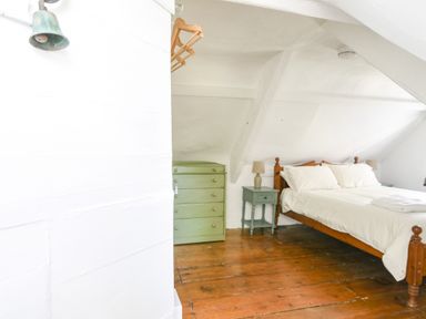 A bedroom with a wooden bed a green chest of drawers a bedside table with a lamp and wooden floors at Braeside in Lyme Regis