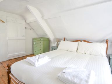 A bedroom with a wooden double bed white bedding towels on the bed a green chest of drawers and a bedside table with a lamp at Braeside Lyme Regis
